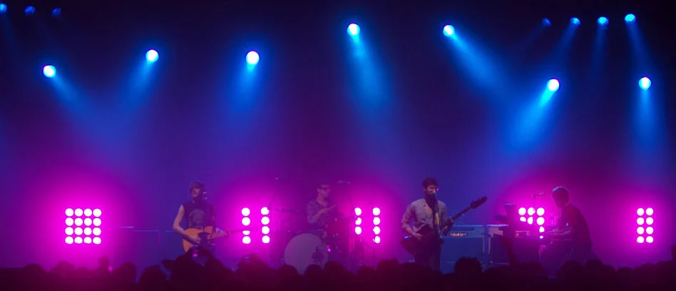 Live band beneath blue spotlights and magenta stage lights