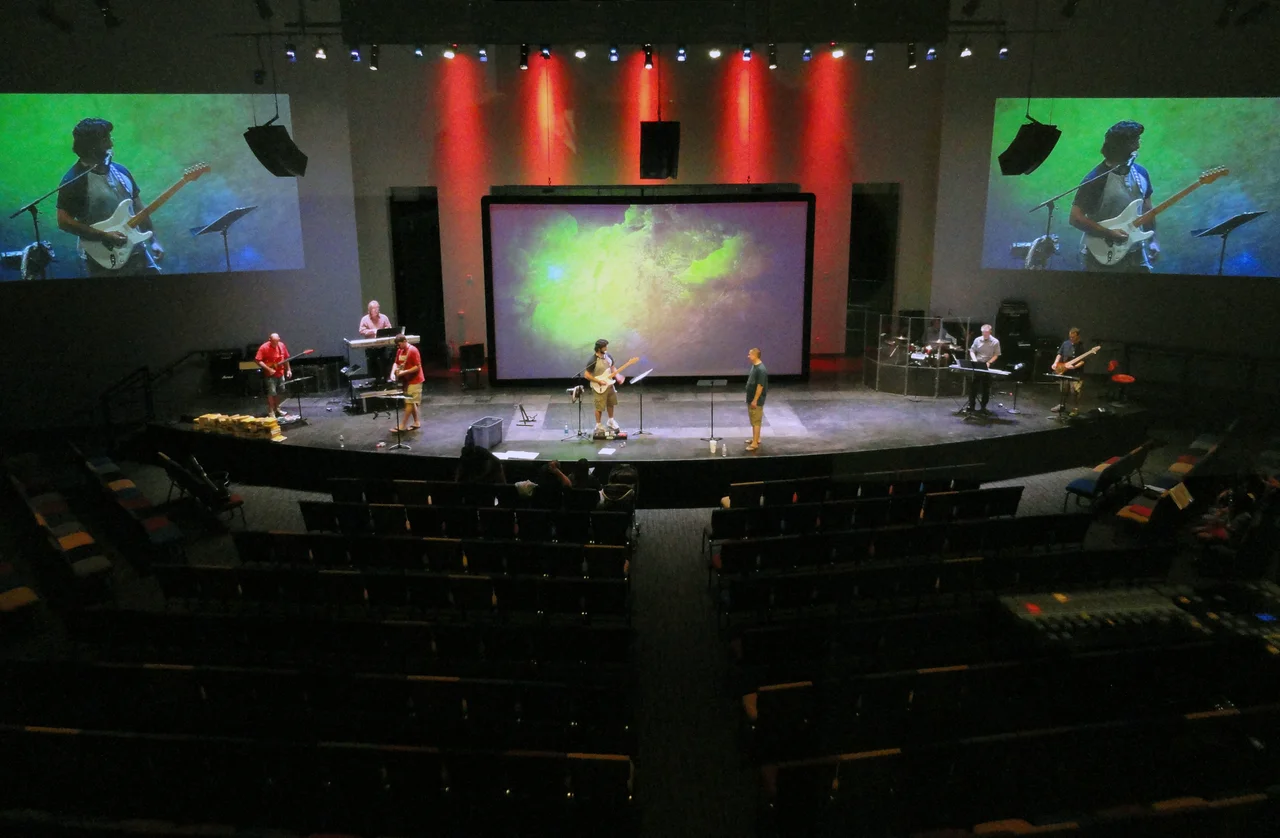 Band rehearsal with large video screens and red overhead lighting
